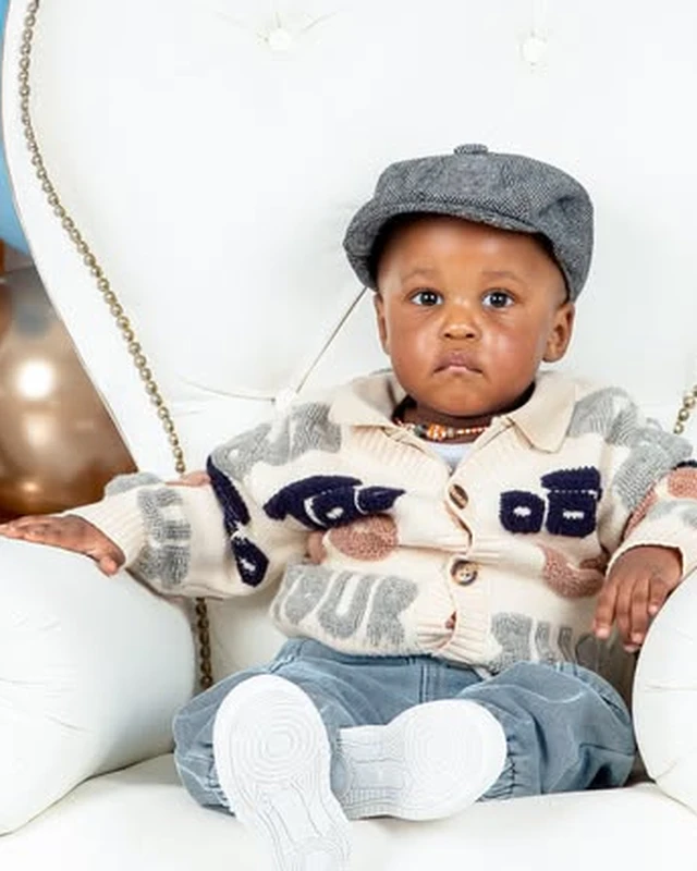 Birthday photoshoot, boy in a flat cap on a white throne chair, blue and gold balloon arch