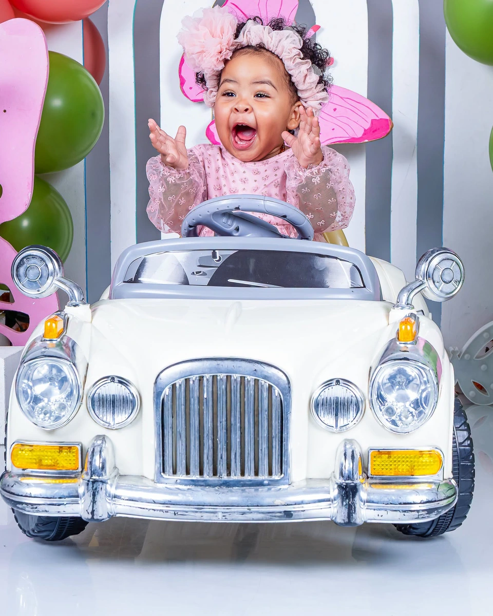 Baby milestone photoshoot, girl in butterfly wings on a toy car